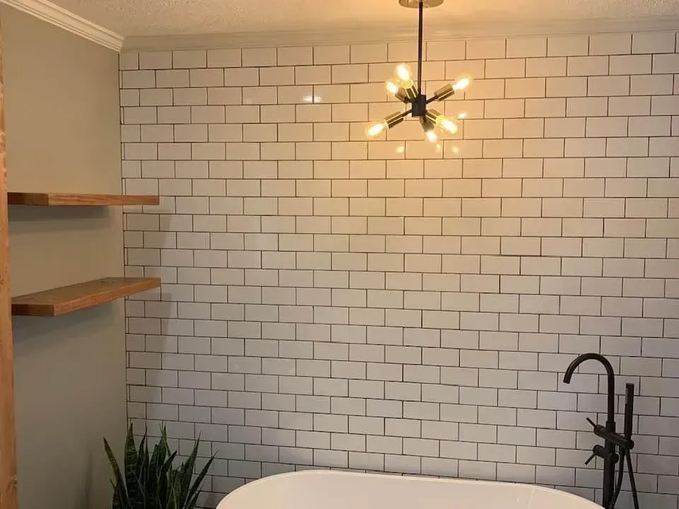 Bathroom with white brick-style wall, floating shelves, black fixtures, and a modern light fixture above a bathtub.
