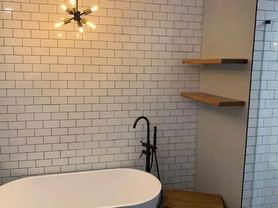 Modern bathroom with white brick-style tile, a freestanding tub, and wooden shelves. Black faucet and shower.