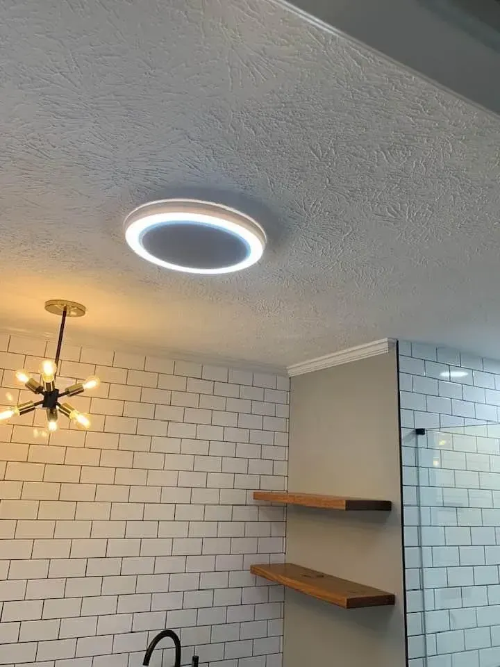 Circular LED ceiling light in a bathroom with brick-like wall and floating shelves.