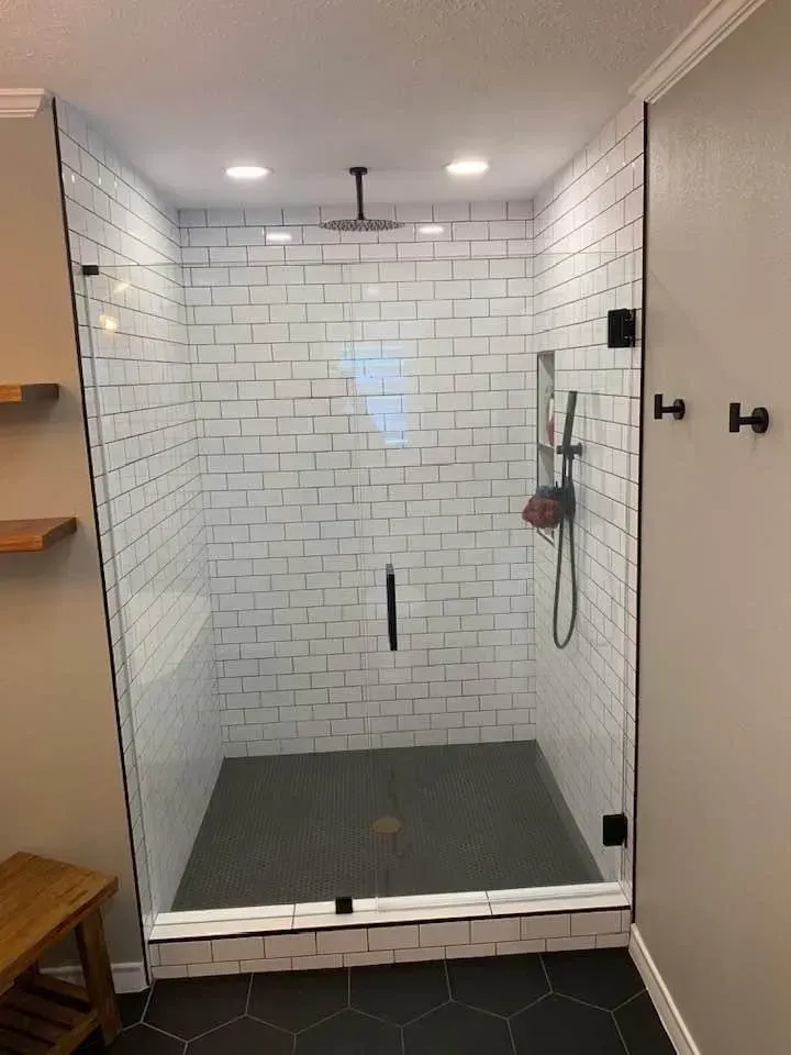 Modern shower stall with white subway tile walls, a dark floor, and glass door.