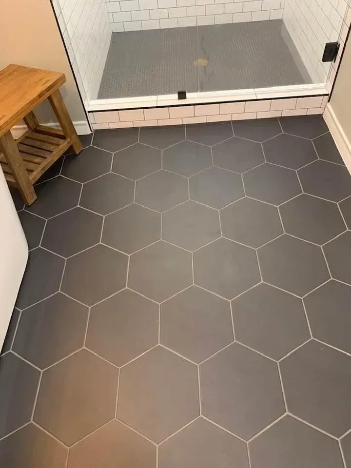 Gray hexagon tile floor in a bathroom, with a shower and wooden stool visible.