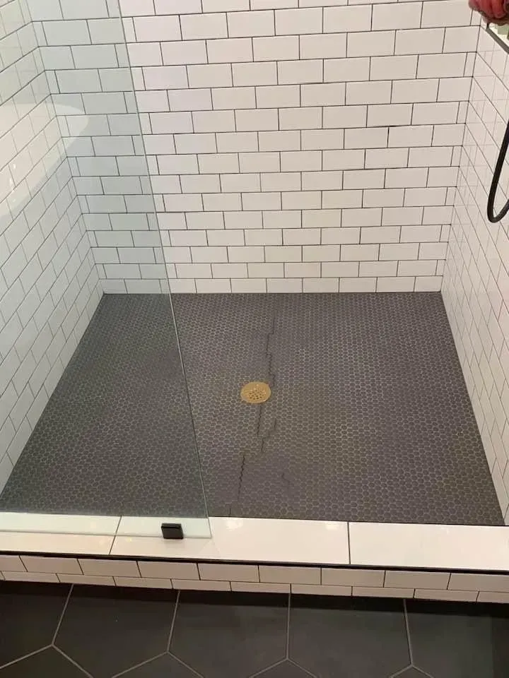 Shower stall with white subway tile walls, dark hexagon tile floor, and glass door.