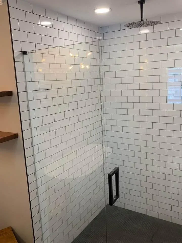 White tiled shower with glass door, black fixtures, and a rain showerhead.