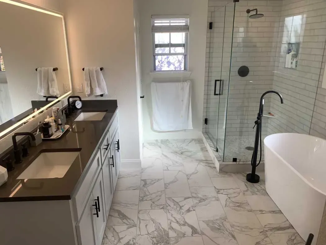 Bathroom with white marble floor, double sinks, a freestanding tub, and a glass shower.