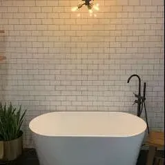 A modern bathroom with a white oval bathtub, subway tile wall, and black faucet.