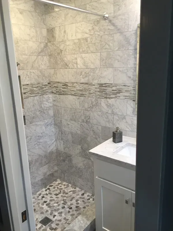 Small bathroom with marble tile shower and pebble floor, white vanity.