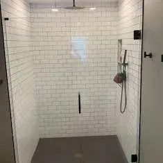 A modern shower with white subway tile walls and a glass door. Grey floor, silver fixtures.