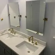 Bathroom with white countertop, two sinks, gold faucets, and mirrors.