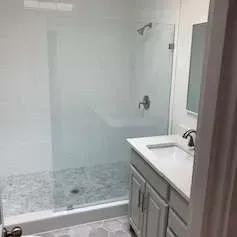 Bathroom with a glass shower enclosure, white vanity, and gray tile floor.