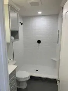 Small, modern bathroom with white shower, toilet, and vanity. Gray floor and cabinets.