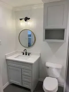 Small gray and white bathroom with sink, mirror, toilet, and cabinet.
