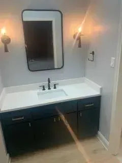 Bathroom with a black vanity, white countertop, rectangular mirror, and sconce lighting.