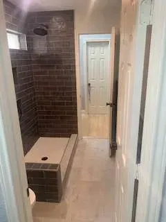 Bathroom with brown tiled shower, white door, and neutral flooring.