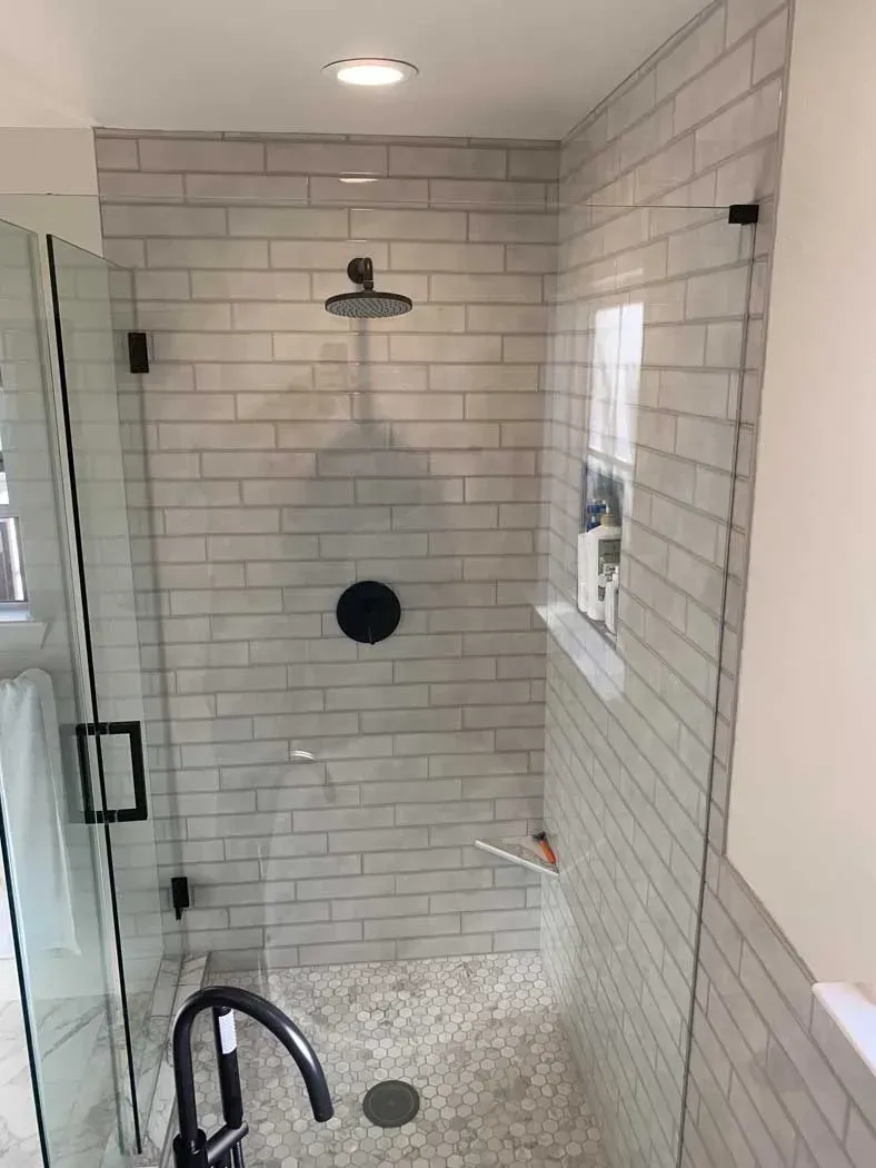Shower with white subway tile, pebble floor, and glass doors with black hardware.