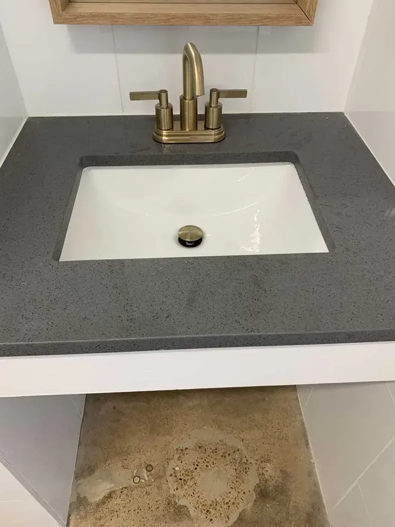 Bathroom sink with grey countertop, white basin, gold faucet, and a mirror above.