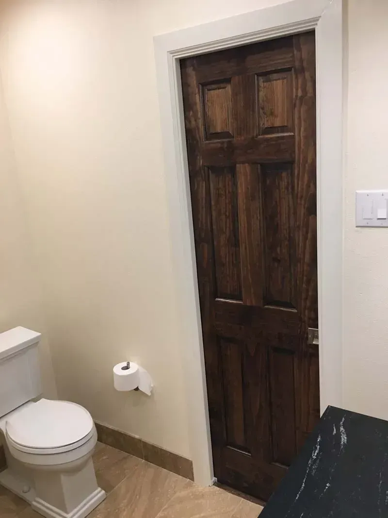 A dark wood bathroom door with white trim, a toilet to the left, and a light switch on the wall.