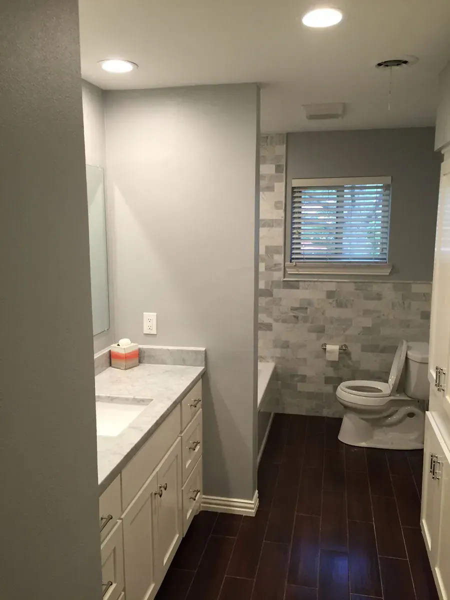 Bathroom with white vanity, toilet, and gray walls, dark wood floor, and window with blinds.