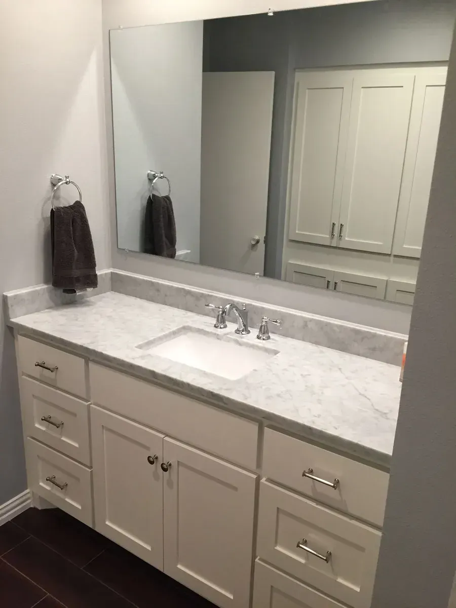 Bathroom with white vanity, marble countertop, large mirror, and towel rack.