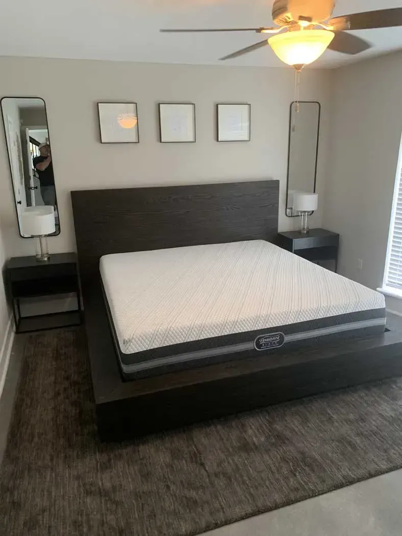 Bedroom with a dark wooden bed frame, mattress, nightstands, and wall mirrors.