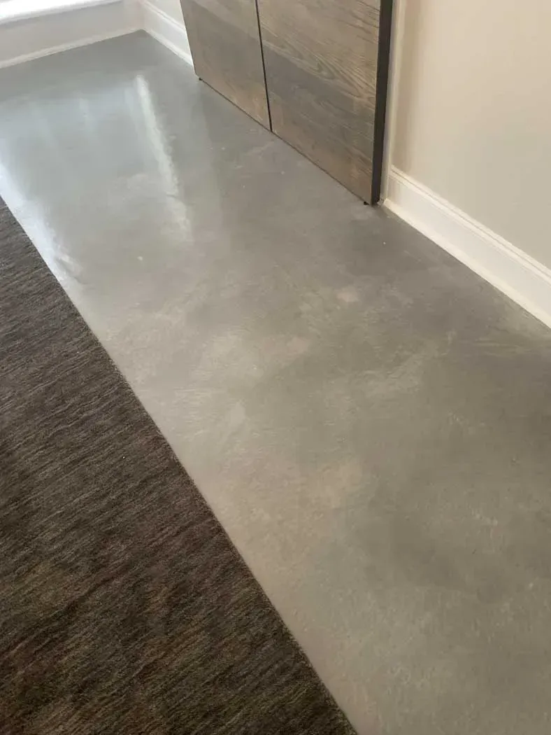 Gray concrete floor with rug on the left and wooden door.