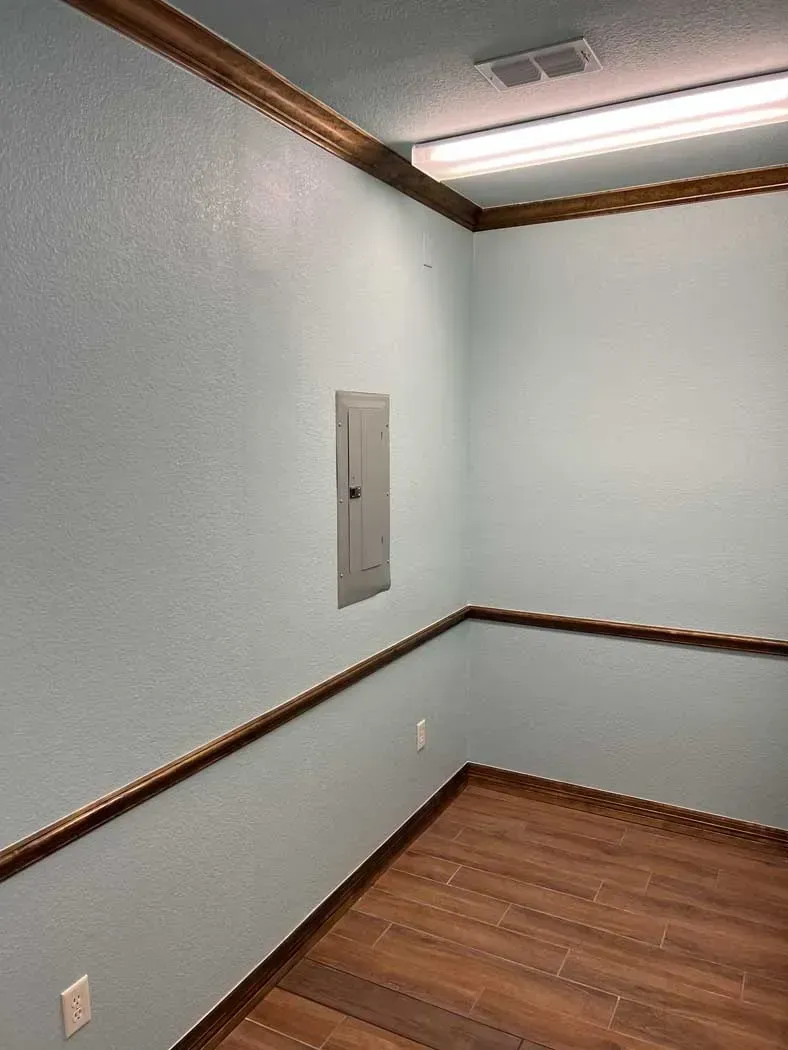 Empty room with light blue walls, brown trim, wooden floor, and electrical panel.