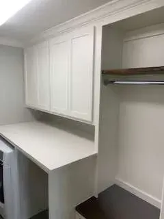 White laundry room with countertop, cabinets, and a hanging rod.