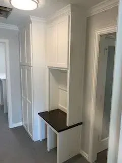 White built-in cabinets with a desk area in a hallway, dark counter, and a doorway.