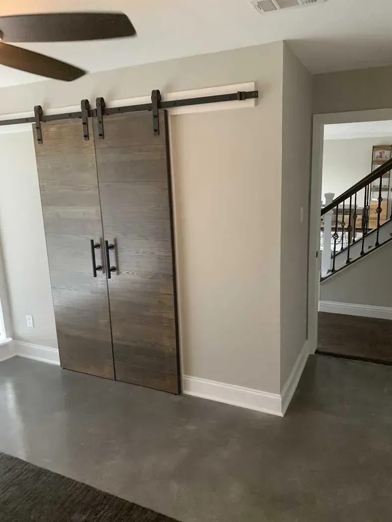 Barn doors, mounted on a track, close off a doorway. The walls are gray, with white trim and a concrete floor.