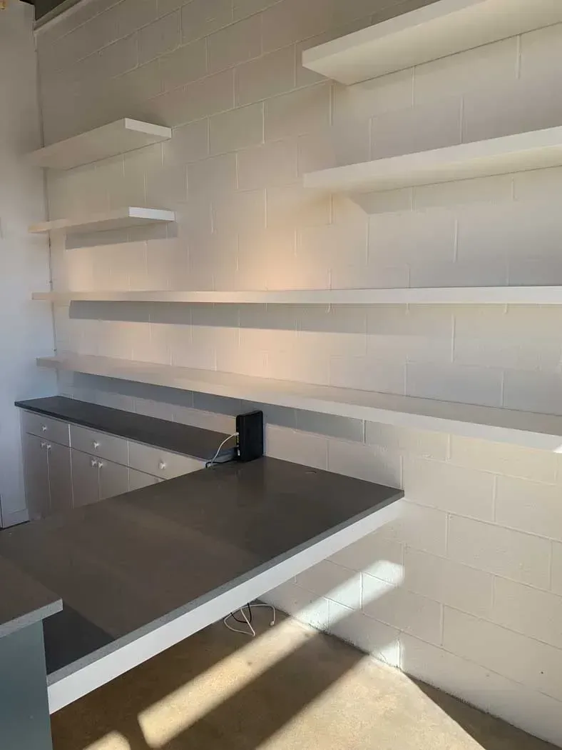 White wall with floating shelves and a built-in countertop, lit by sunlight.