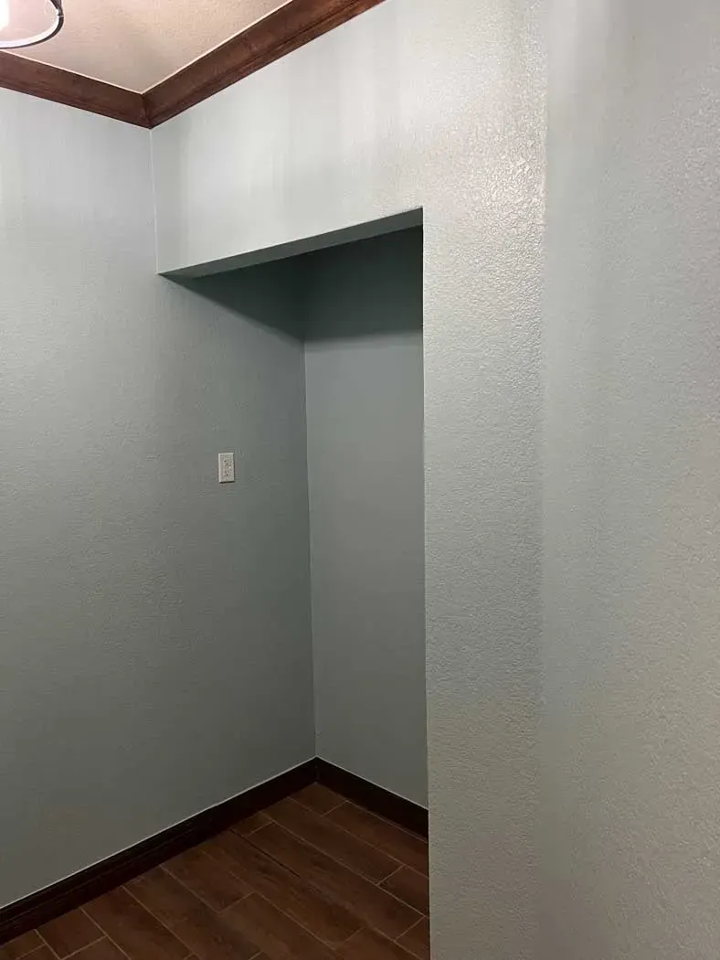 Empty, blue-painted room with a recessed alcove, brown trim, and wood-look flooring.