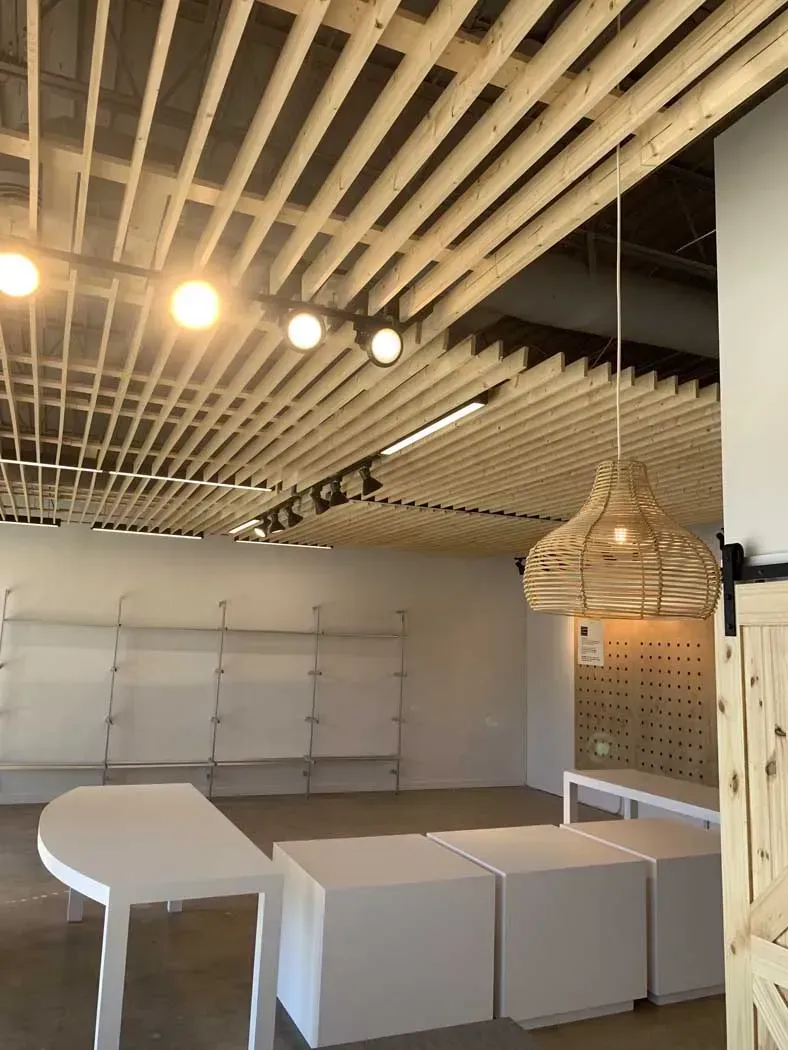 Empty retail store with wood slat ceiling, pendant light, display tables, and shelving.