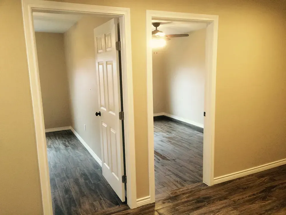 Two doorways, one with a closed white door, lead into rooms with wood-look flooring and beige walls.