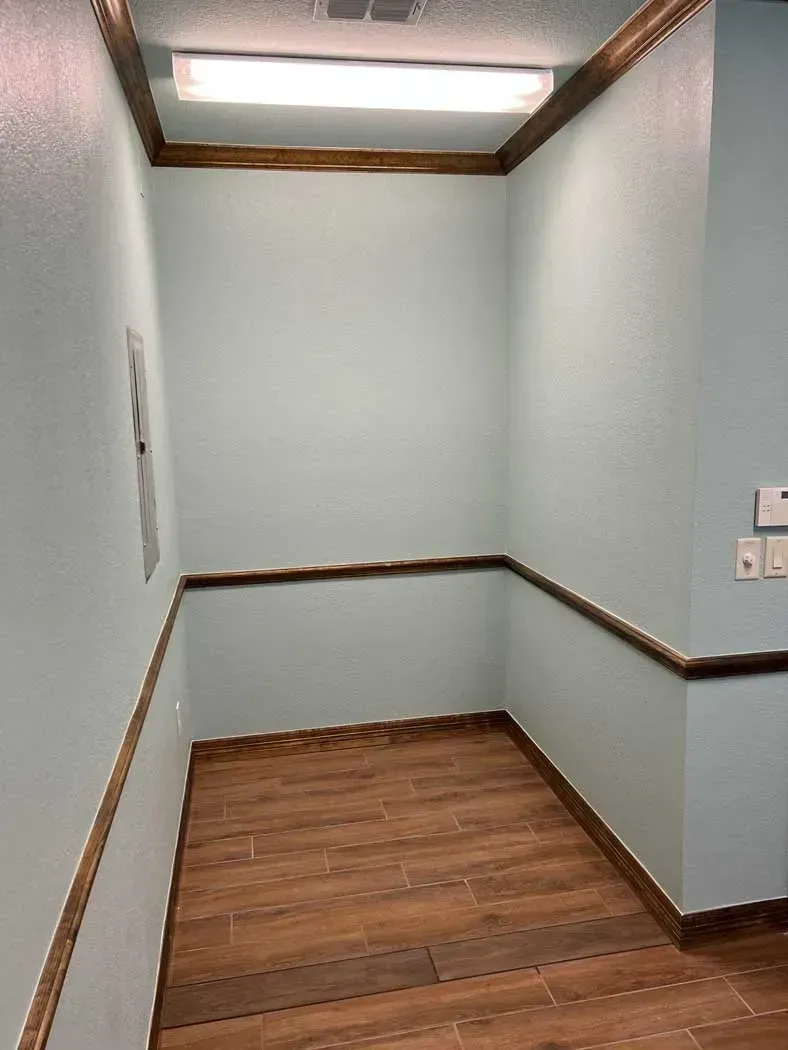 Small, empty room with light blue walls, brown trim, and wood-look flooring.
