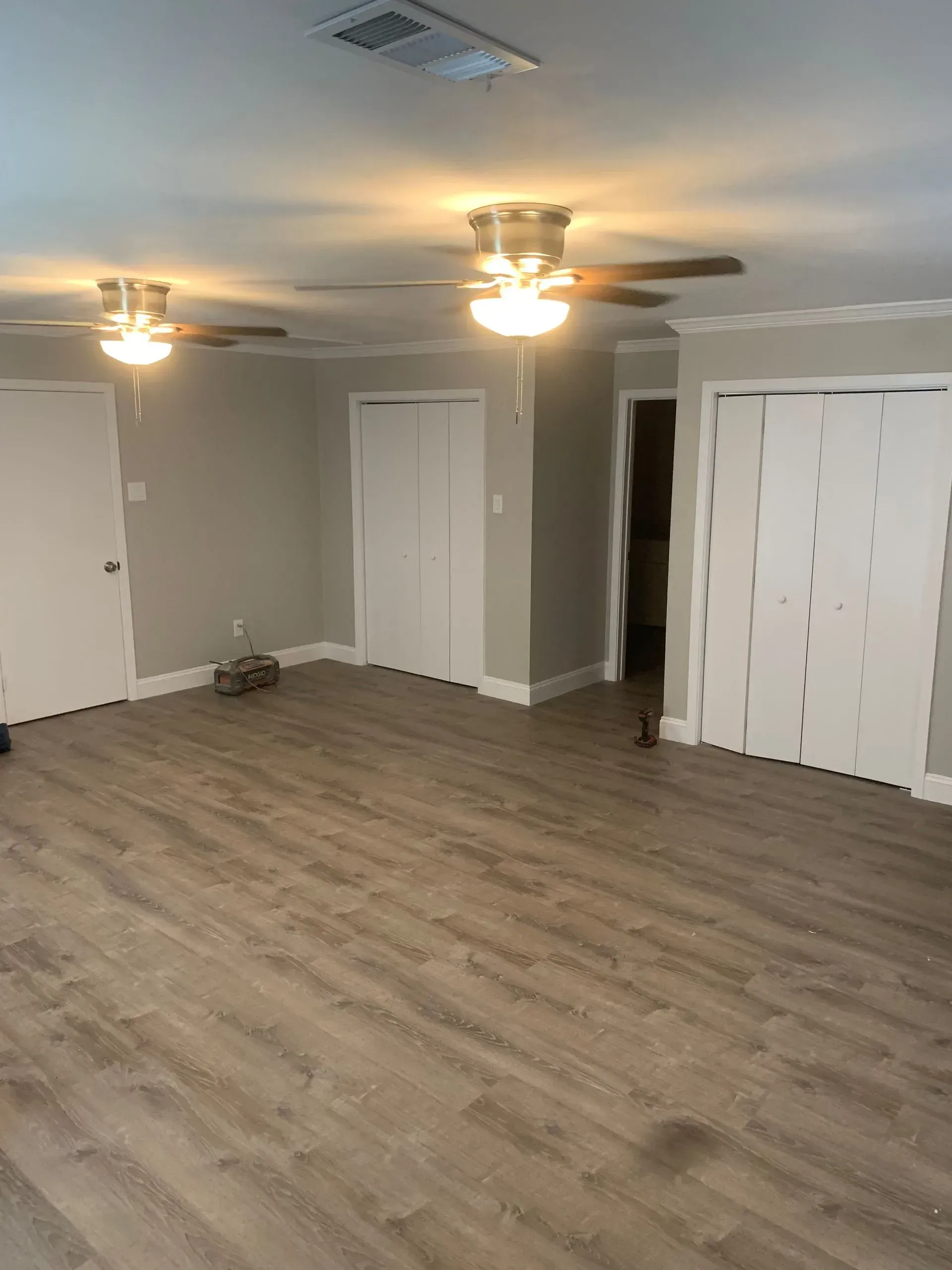 Empty room with light wood-look flooring, gray walls, white trim and doors, two ceiling fans with lights.