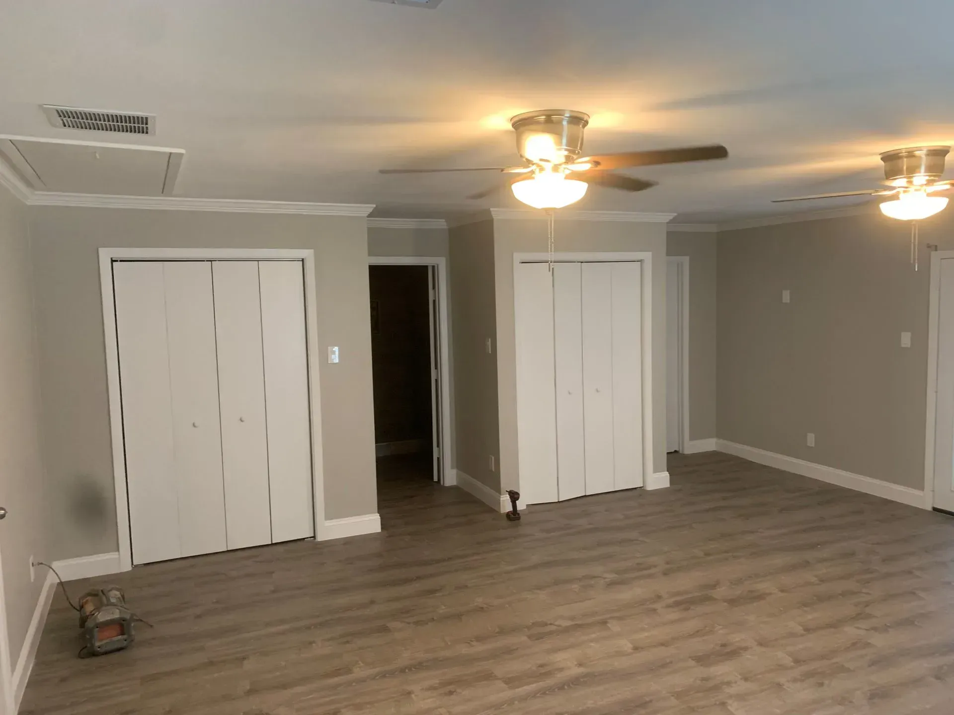 Empty room with two closets, light gray walls, white trim and doors, two ceiling fans, and wood-look flooring.