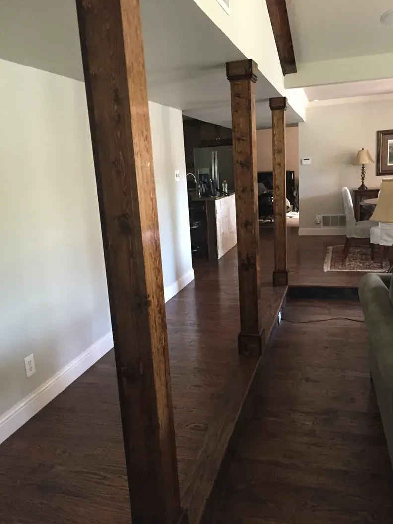 Wooden columns supporting a ceiling in a room with hardwood floors.