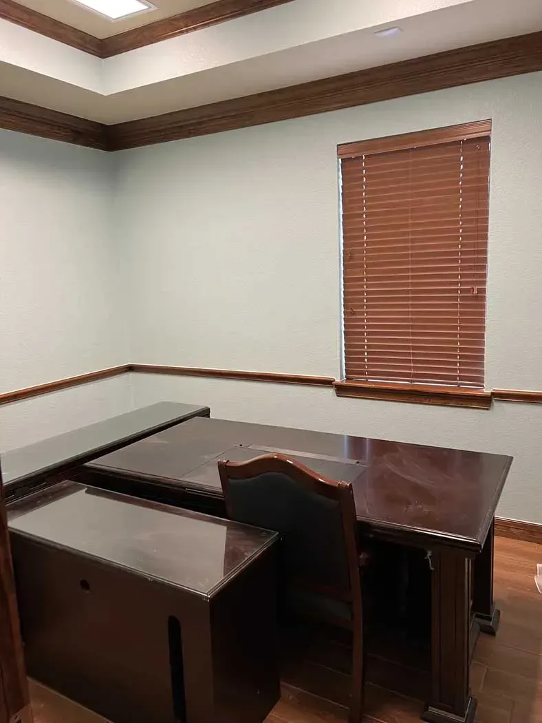 Office room with wooden desk, chair, and blinds against light blue walls and brown trim.