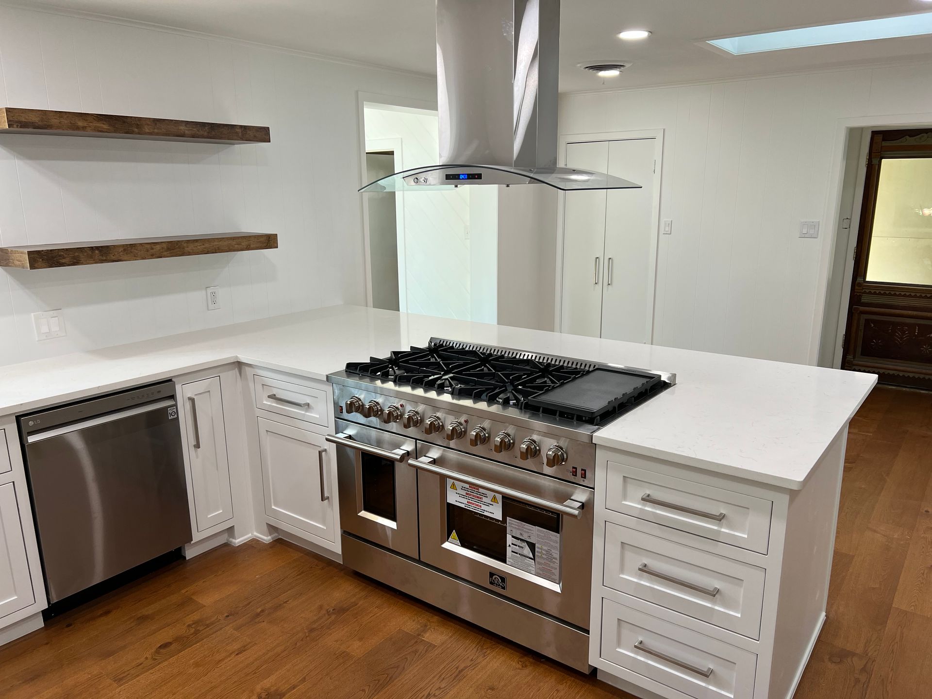 Modern kitchen with stainless steel appliances, white cabinets, and wooden shelves.
