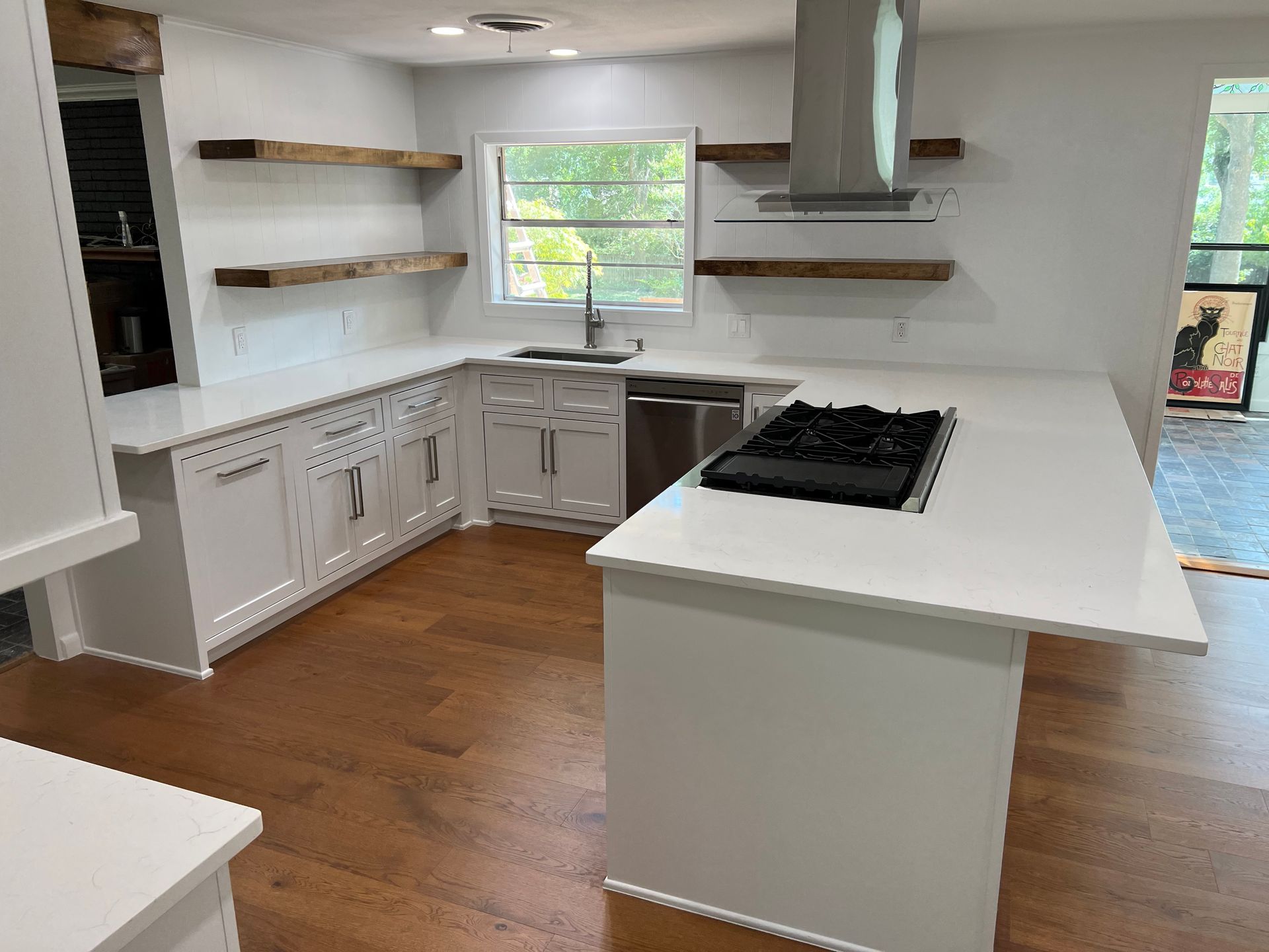 Modern white kitchen with island, wooden shelves, and stainless steel appliances.