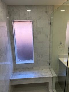 Shower with marble tile, glass door, built-in bench, and window.