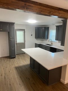 Kitchen with gray cabinets, white countertop, and wood-look flooring. A dark brown beam is overhead.