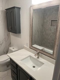 Bathroom with white quartz countertop, gray cabinets, large mirror, and a white toilet.