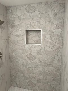 Shower wall with stone-like gray tiles, built-in shelf, and chrome fixtures.