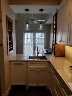 Small kitchen with white cabinets, light countertop, sink, and view of exterior through double doors.