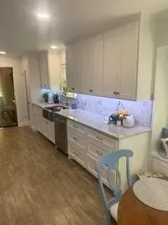 White kitchen cabinets and counters, stainless sink, and light wood floors.
