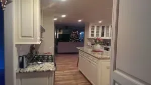Kitchen interior with white cabinets, island, and appliances, open to a living area with a Christmas tree.