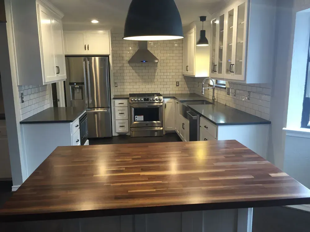 Modern white kitchen with a stainless steel refrigerator and range, black countertops, and a wooden island.