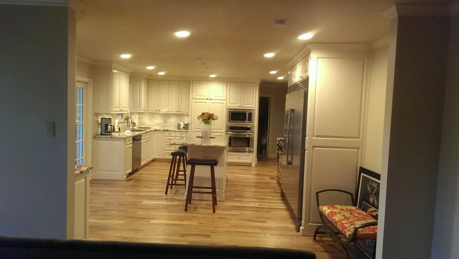 Bright kitchen with wood floors and white cabinets, including an island with stools and a stainless steel refrigerator.