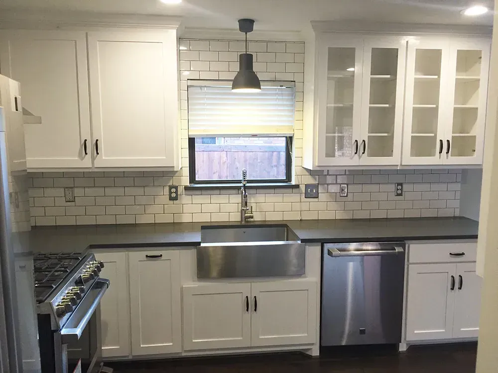 White kitchen with stainless steel appliances, dark countertops, and subway tile backsplash.