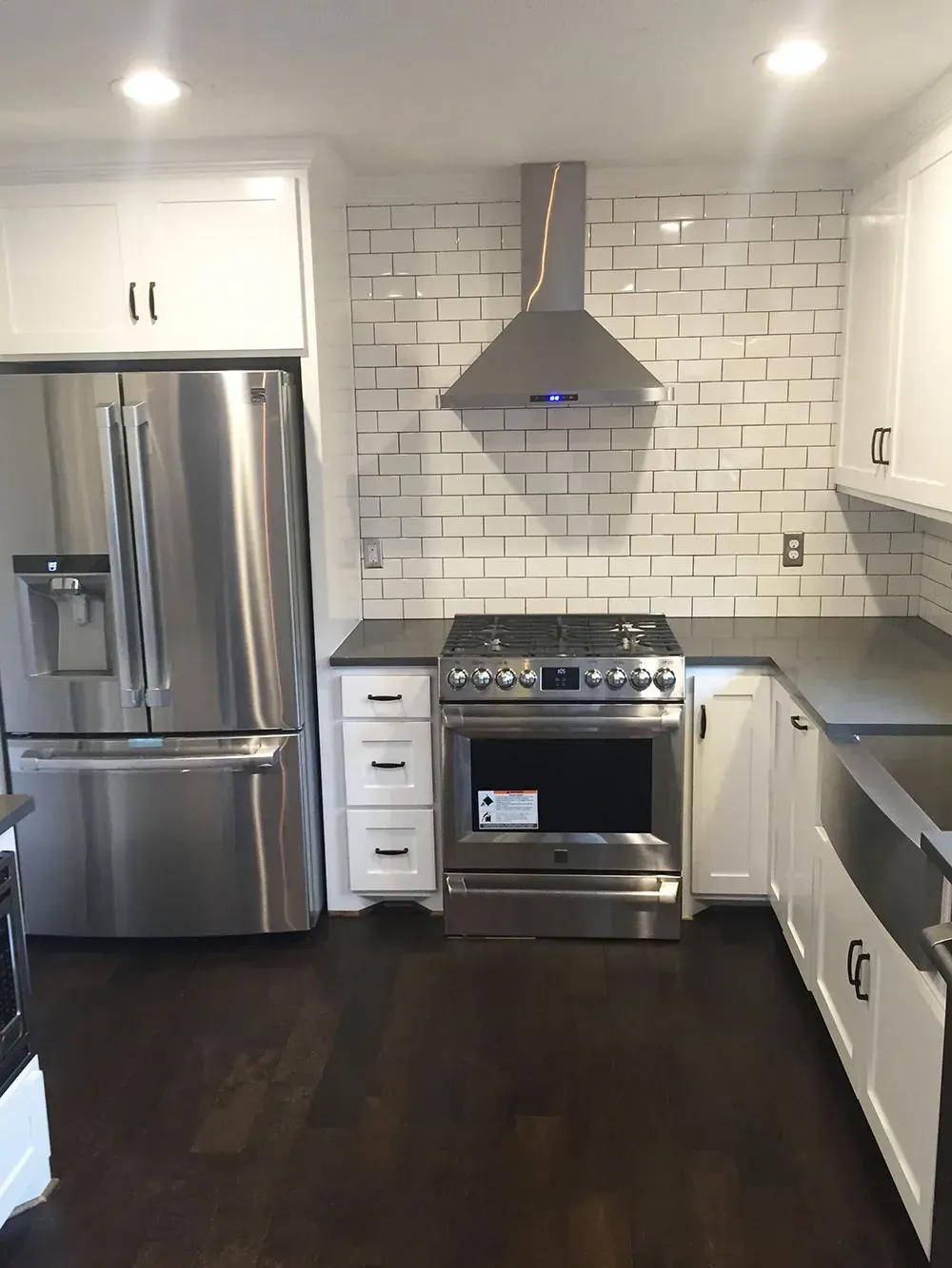 Modern kitchen with stainless steel appliances, white cabinets, brick backsplash, dark countertops and floors.